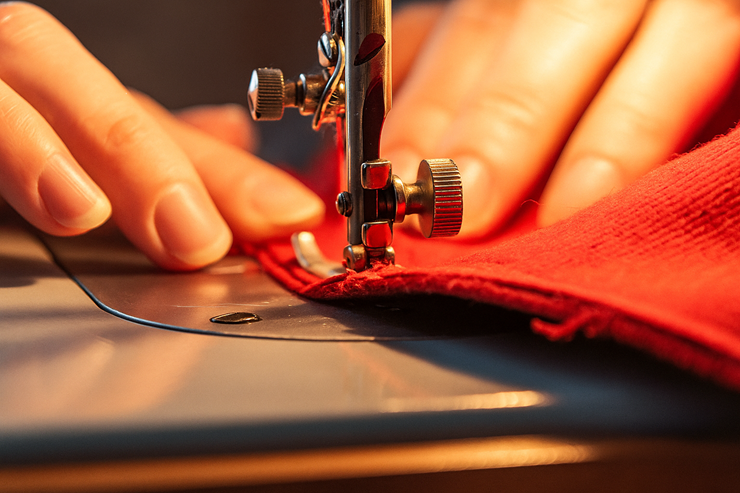 Close-up of hands sewing red fabric on an industrial machine during sofa upholstery repair